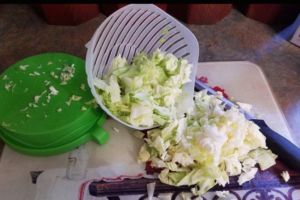 sliced salad in bowl with green lid spilling on counter