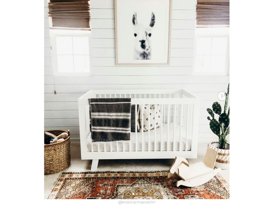 shiplap wall in nursery with huge llama artwork two windows a white crib and vintage style rug