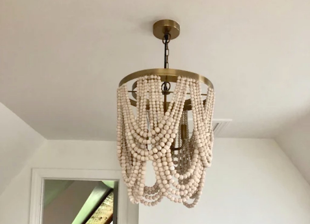 wood bead chandelier with gold accents hanging from white ceiling