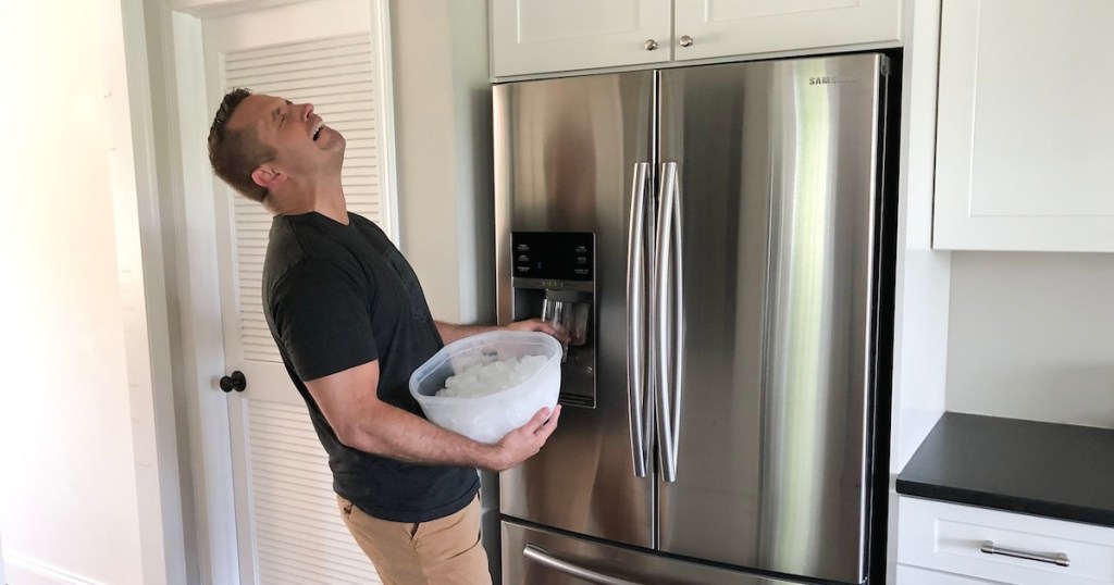 frustrated man holding an ice bucket in front of stainless steel refrigerator holding glass