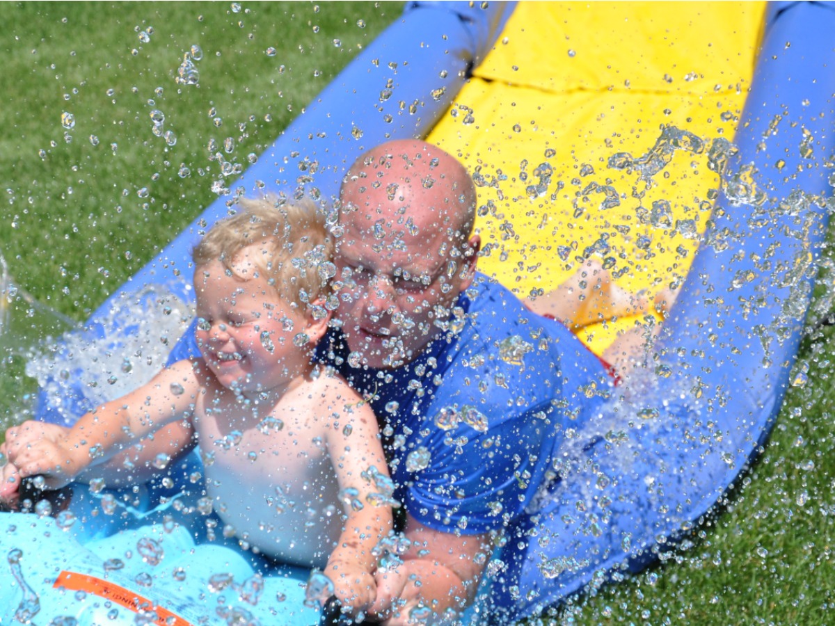 Dad and son sliding down a long PVC slide in grass