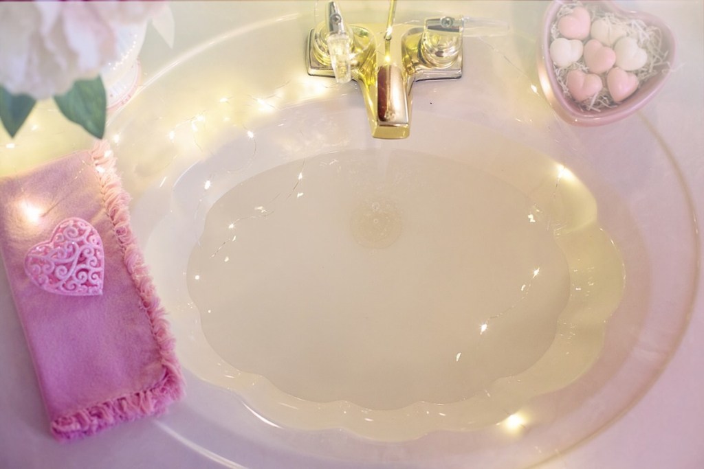 white shell shaped sink with gold faucet and pink accents