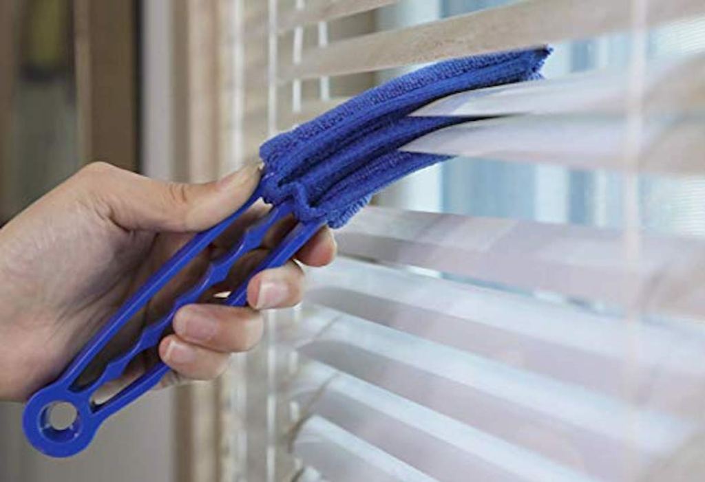 hand holding blue blind duster cleaning white blinds