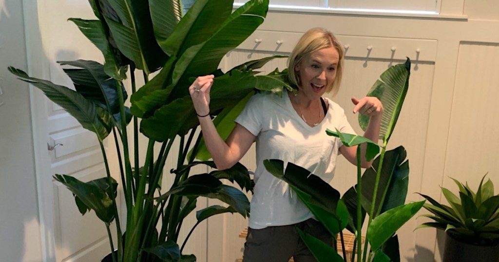 woman standing in the middle of two plants - one real and one fake 