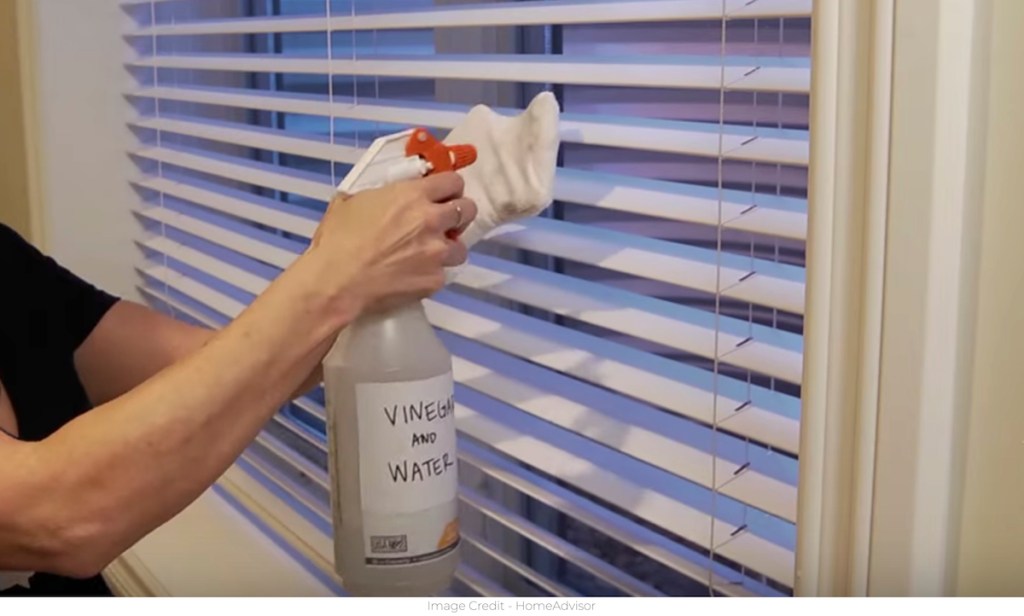 hand with white sock and spray bottle cleaning blinds
