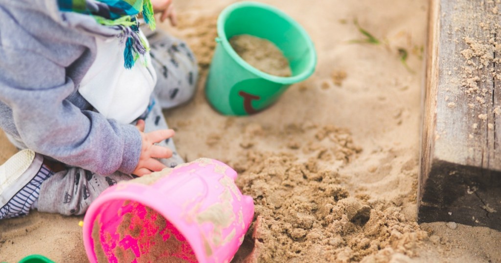 Child playing in a sandbox with plastic buckets 