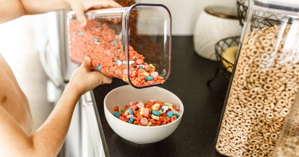 kid pouring pink lucky charm cereal into white bowl