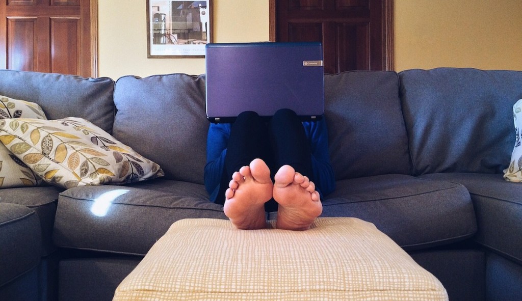 person with laptop sitting on blue couch 