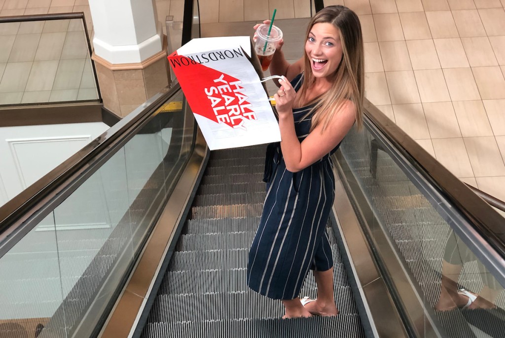 woman going down escalator with shopping bag and drink